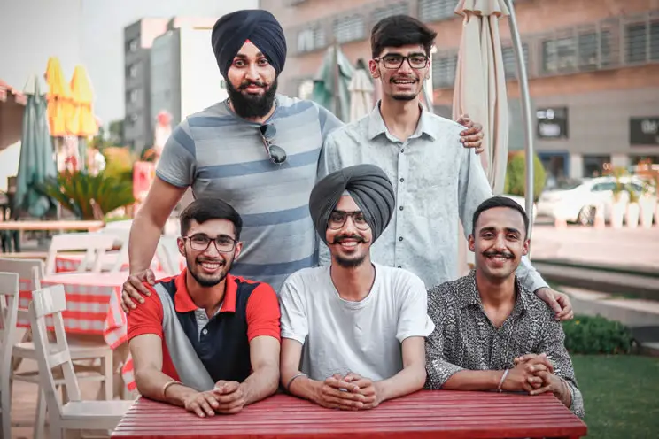 Group of Sikh men sat around table looking at the camera