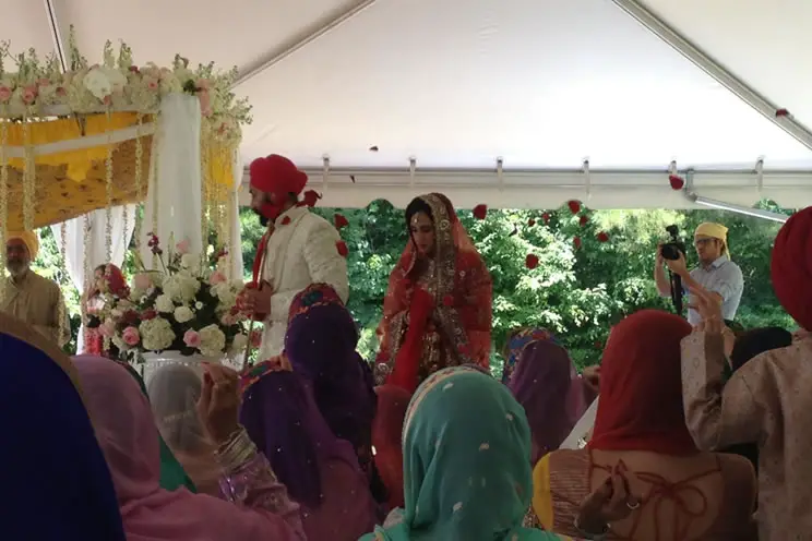 Sikh groom being followed by Sikh bride around holy book in outdoor sikh wedding.