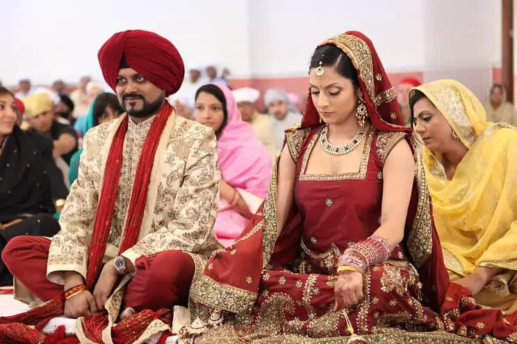 Sikh groom and bride sitting cross legged in front of the mahraj where the holy book the guru granth sahib resides